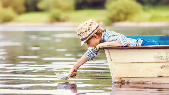 boy launches paper boat on a lake vacation