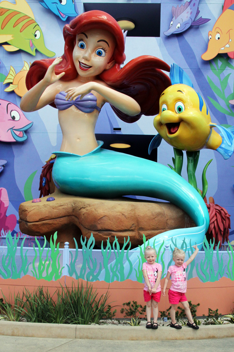 Two girls get their picture taken in front of a giant statue of Ariel and Flounder in the Little Mermaid Section of Disney's Art of Animation Resort