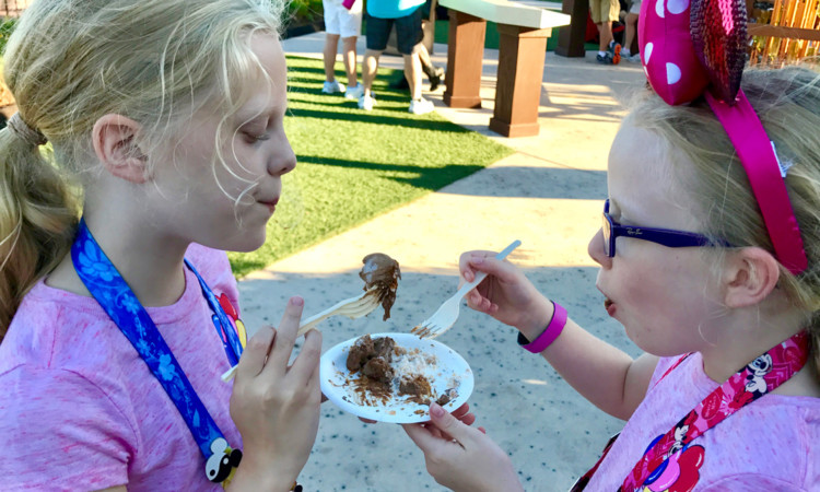 two young girls enjoy a sample of kid-friendly food at the Epcot International Food and Wine Festival