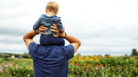 baby on dad's shoulders looking over green grass and ocean
