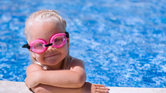 Toddler girl wearing swim goggles in a swimming pool