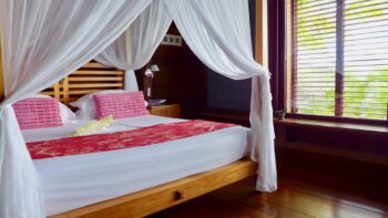 king size bed draped with mosquito netting in caribbean beach house